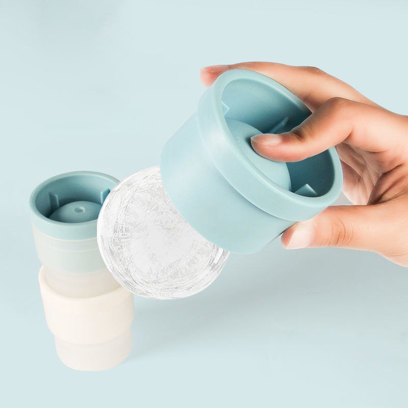 A hand squeezing a silicone mould to release a round ice sphere